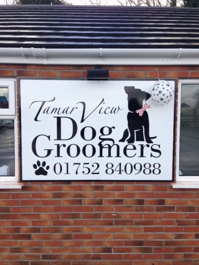 The hanging sign outside the grooming shop on its brick and pebbledash wall